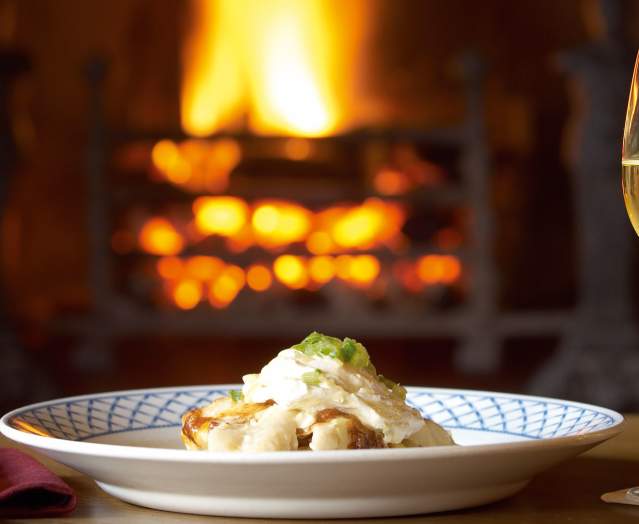 plate of food beside an open fire with a glass of wine