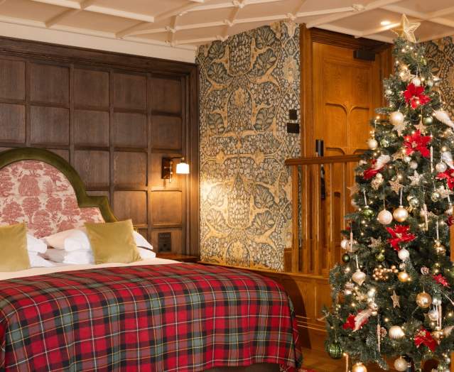 A bedroom at The Old Inn, featuring a double bed with a tartan bedspread and a brightly decorated Christmas tree beside it.