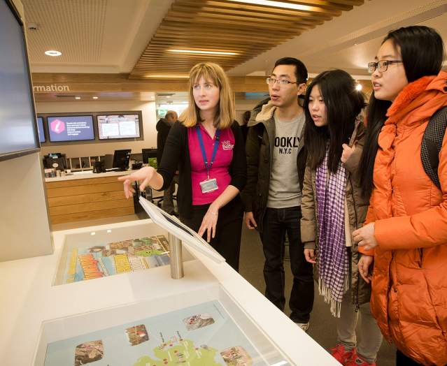 An employee showing tourists how to use some of the touch screens inside Belfast Visitor Centre