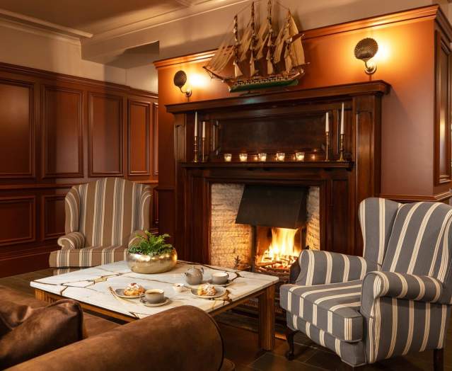 Cosy scene at The Harbourview Hotel with a roaring open fire, chairs in front and tea and scones on the table.