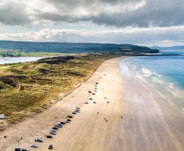 Aerial view of Portstewart beach with cars parked along the stretch of sand.