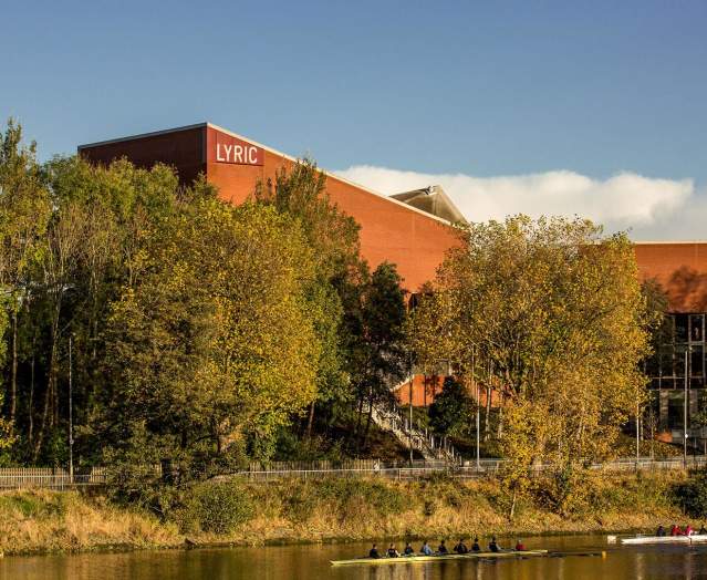 Exterior of The Lyric Theatre in Belfast on a sunny day with rowers on the river beside it