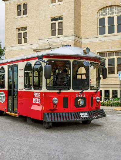 Downtown McKinney Trolley - red and beige - on front of large cream colored building