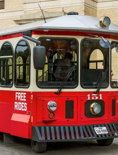 Downtown McKinney Trolley - red and beige - on front of large cream colored building