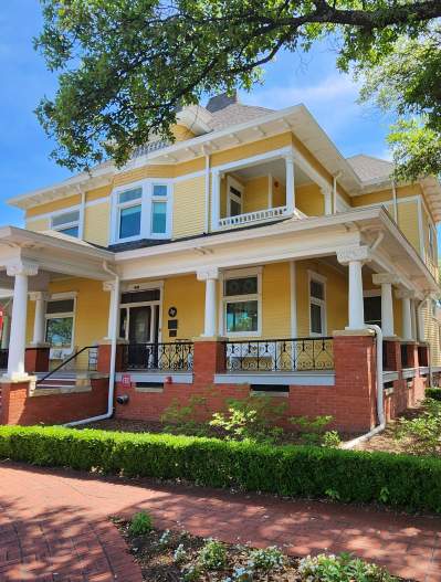 Big yellow house with hedge around red brick sidewalk leading to steps