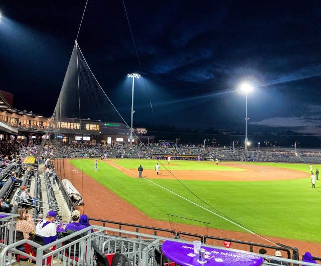 Stadium seating and playing field under bright lights during an evening sporting event, illustrating environments where lighting or sound levels may vary throughout an event.