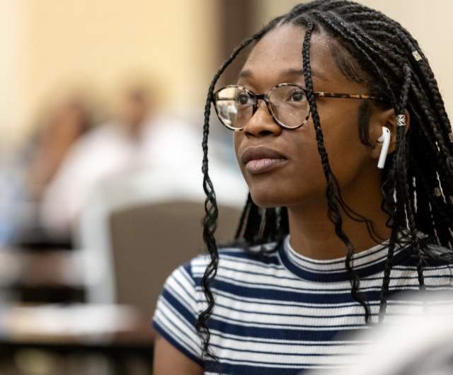 Event attendee wearing noise-reducing earbuds while seated in a meeting room, illustrating personal comfort supports used in group settings.