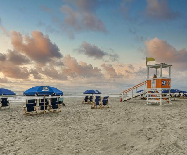 A beautiful sunrise in North Myrtle Beach with beach chairs, umbrellas, and lifeguard stand.