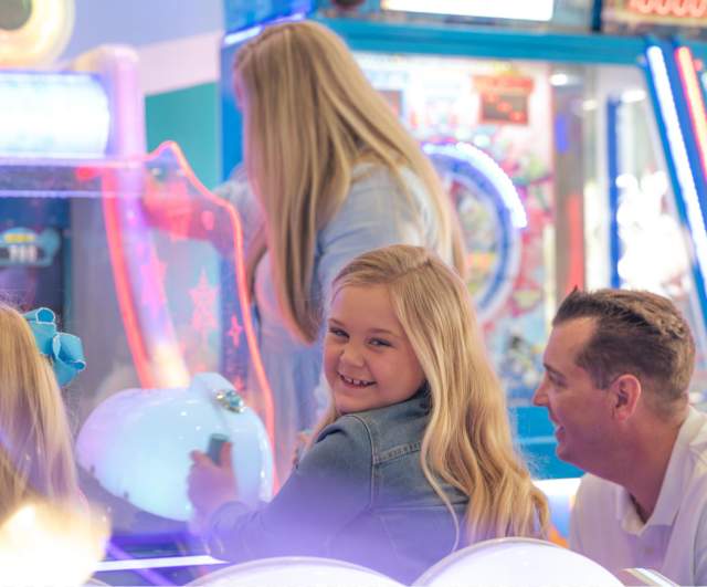 young girl playing an arcade game with her family watching.