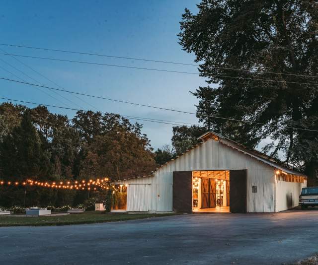A warmly-lit white barn-style tasting room at sunset