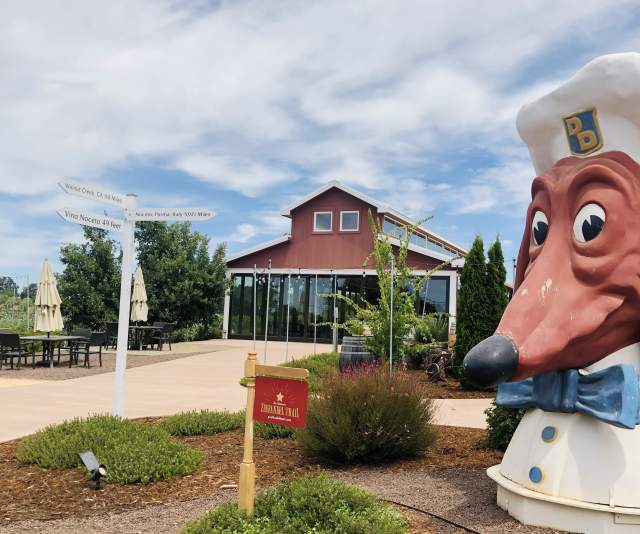 A red barn style winery tasting room under a blue sky streaked with clouds