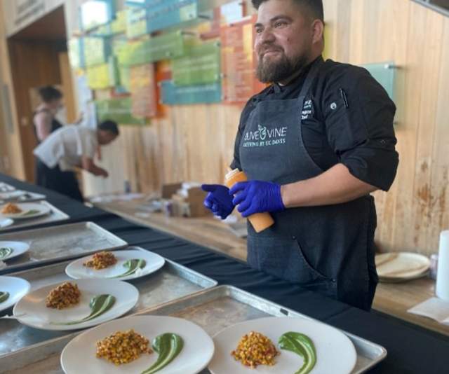 A chef in a black coat and apron preparing plates