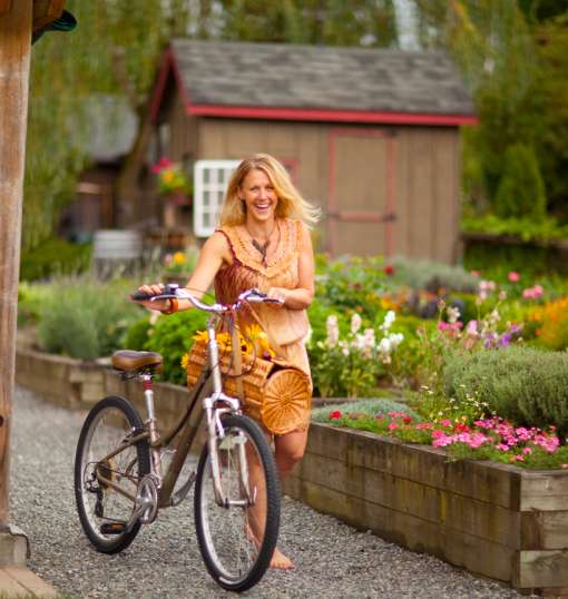 woman in orange dress walks bikes past garden