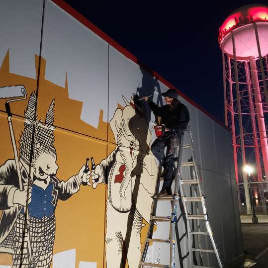Artist on ladder painting mural with old water tower in background