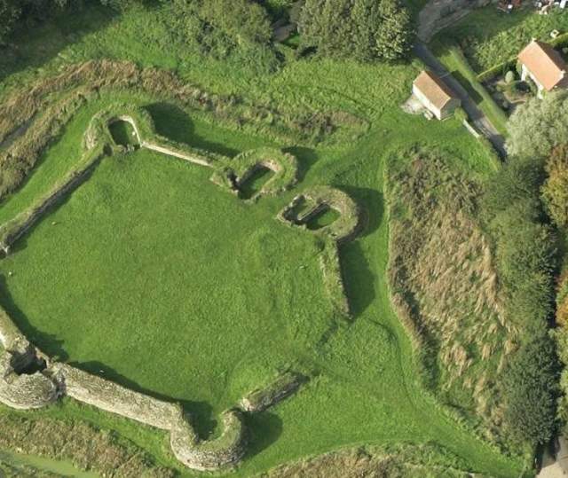 grounds of a castle ruins surrounded by grassy mounds from a drone