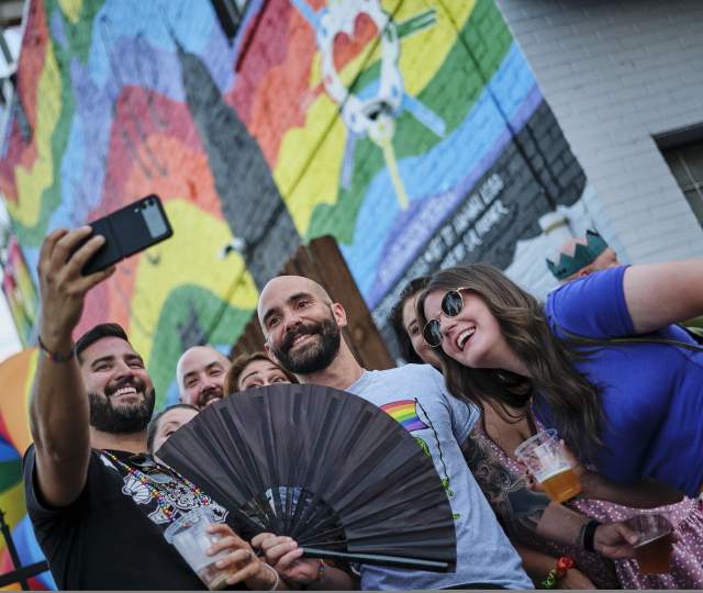 group of people taking a selfie in front of a rainbow mural
