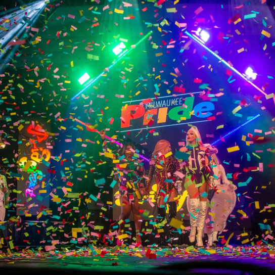 A group of drag queens performing onstage at Pridefest in Milwaukee as party streamers fall around them
