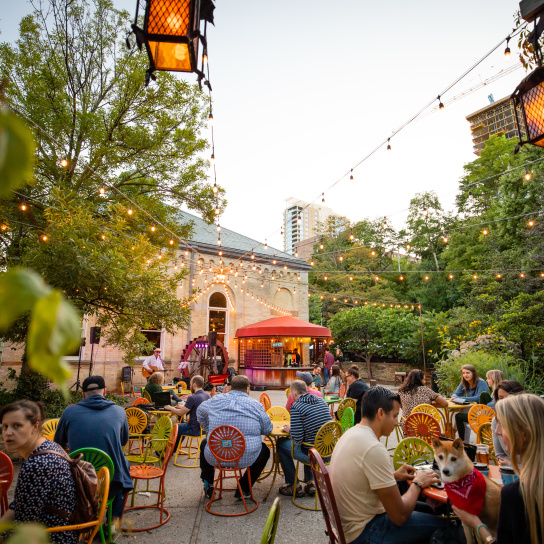 Lively outdoor patio at Colectivo Coffee on the Lake with colorful chairs, string lights, trees, and people dining under evening light.