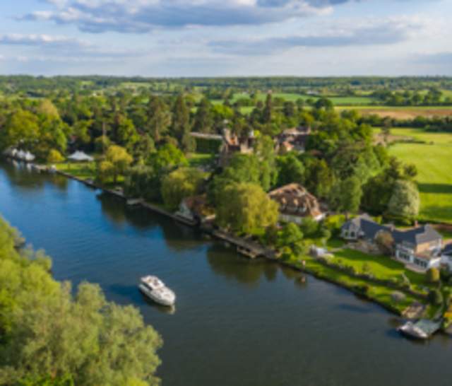 a boat cruising along the river thames surrounded by countryside.