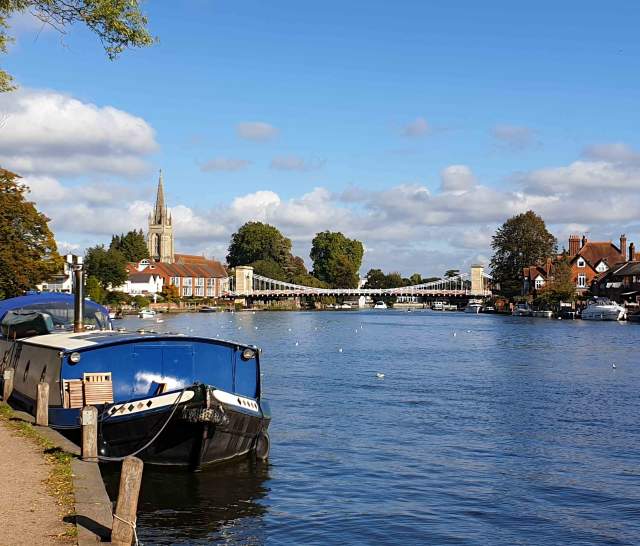 The Thames Path alongside the river Thames with a barge moored and Marlow Bridge and church in the background.