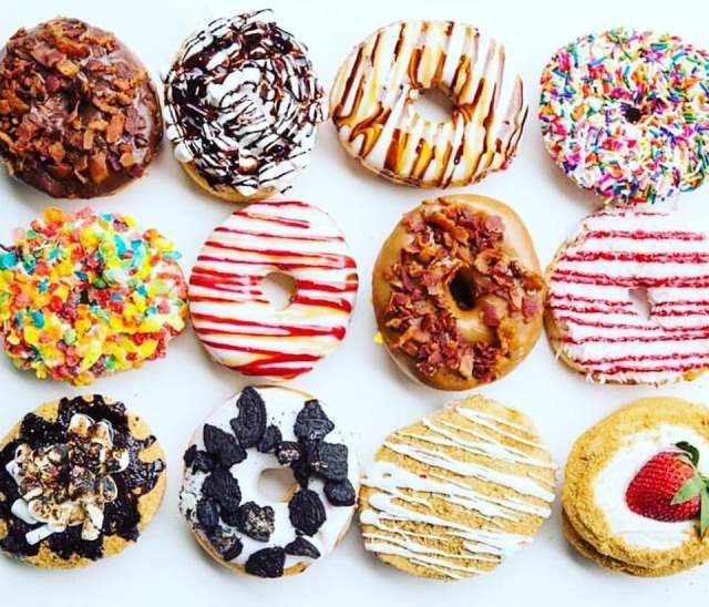 A dozen donuts with different glazes and toppings viewed from above.