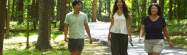 Three individuals walking along trail with trees in background, two have white shirts and one has black shirt.