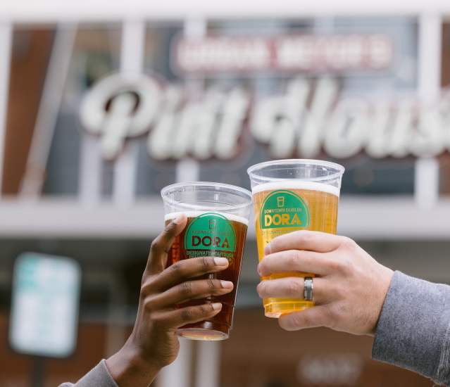 Two DORA cups cheersing in front of Urban's Pint House