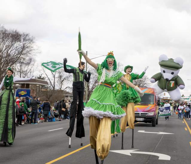 A group of stilt walkers dressed in green performing down the street in the St. Patrick's Day Parade.