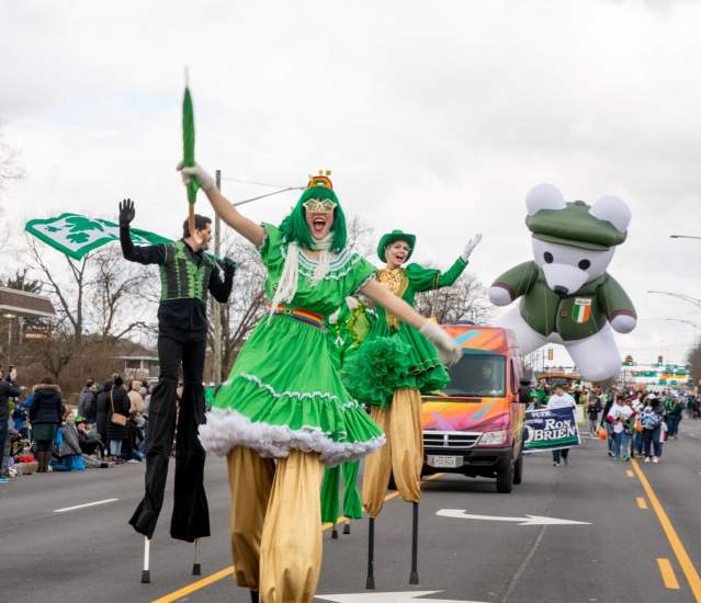 A group of stilt walkers dressed in green performing down the street in the St. Patrick's Day Parade.