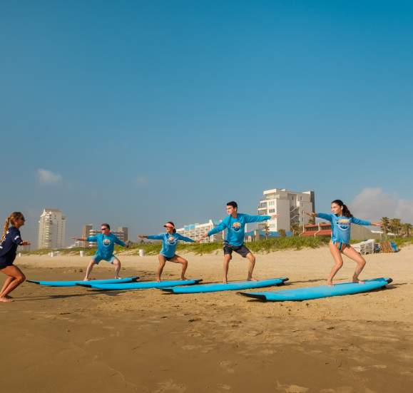Group of young adults on surfboards on the shore being taught a lesson