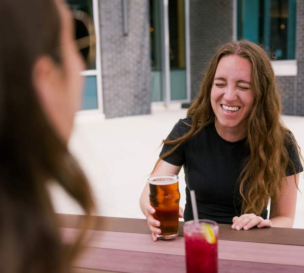 Girls laughing over drinks at an outside picnic table at Strang Hall.