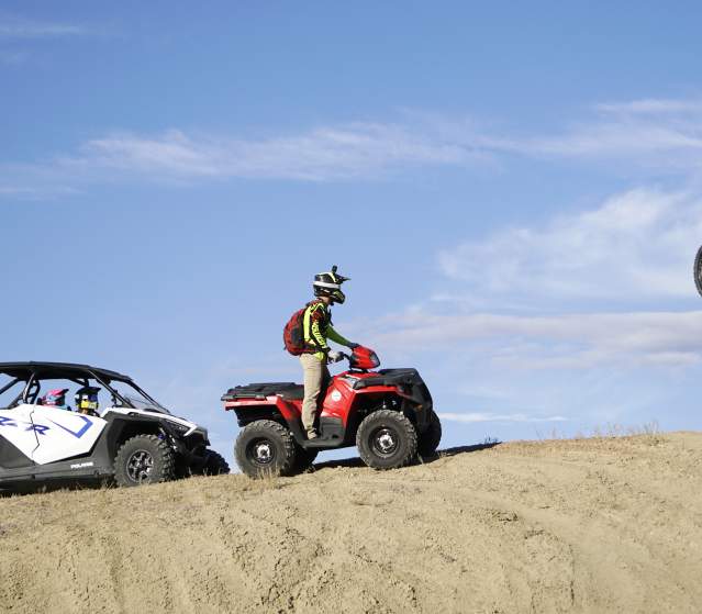 Dirtbiker jumping while people on a fourwheeler and RZR watch