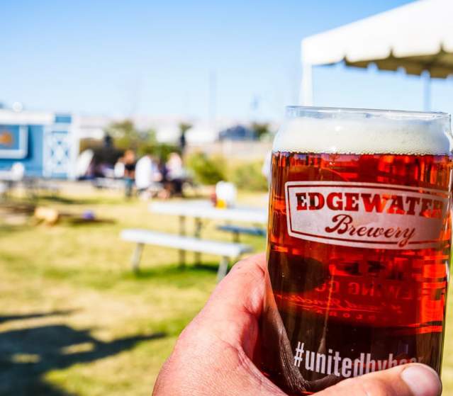 Beer being held with outdoor seating area in background at Edgewater Brewery