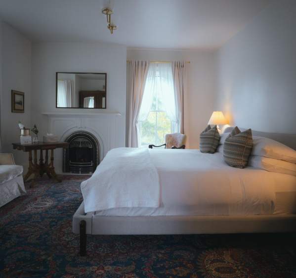 Artisan styled bedroom with fireplace in right corner. Draped curtains exposing daylight.