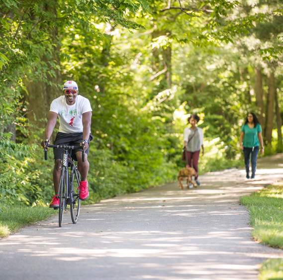 Man riding bike and women walking along wooded rail trail