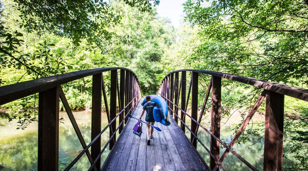 A woman carrying a kayak over a bridge at the Powers Island unit of the Chattahoochee River National Recreation Area.