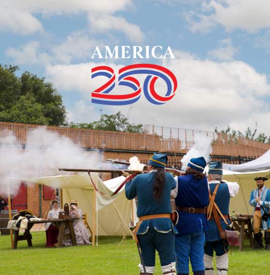 Photo of Historical reenactors firing muskets during Founder's Day at Colonial Fort Conde in Mobile, AL with the official "America 250" logo placed in the sky. The logo features the word "AMERICA" in white text over a red and blue "250"