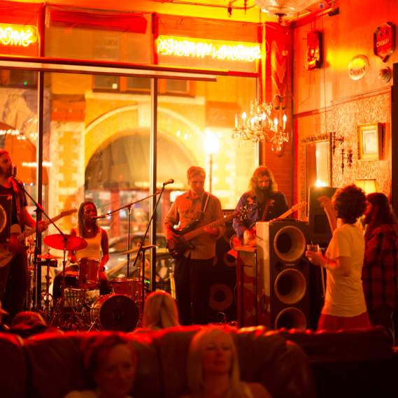 4 piece band performing on stage against bar window at night