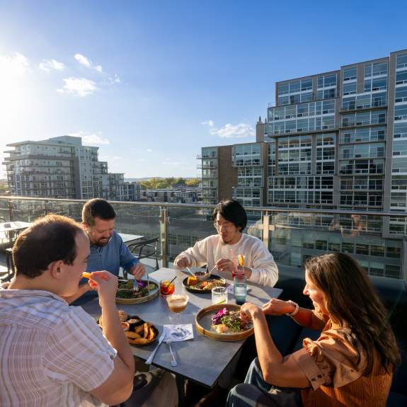 A group of friends enjoy their food while dining on a rooftop restaurant's outdoor patio.