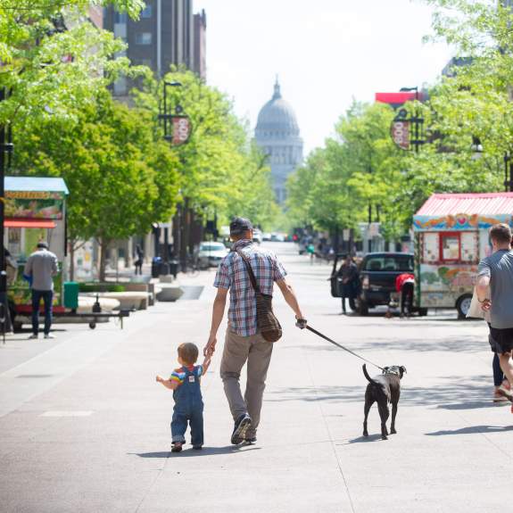 A man and child walking a dog down State Street in Madison