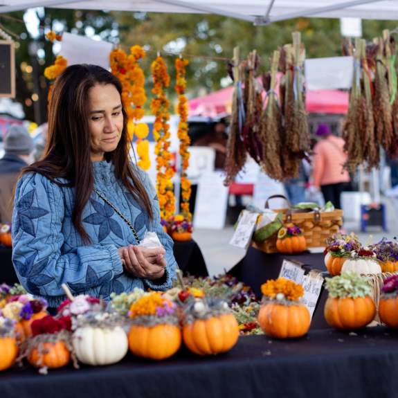 A woman looks at a table of flower arrangements made inside of small pumpkins at the Dane County Farmers' Market