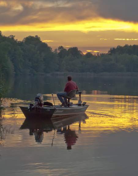 A fisherman enjoys the morning sunrise over the water at Lums Pond State Park.