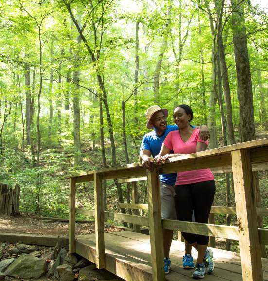 A Couple Standing On A Bridge In A Forest at Big Trees In Sandy Springs