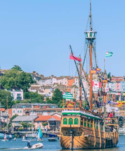 The Matthew ship sailing eastwards along Bristol Harbourside with paddleboarders and the colourful houses of Cliftonwood in the background during the Bristol Harbour Festival - credit Jim Cossey