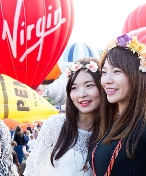 Two women wearing flower crowns standing in front of ascending balloons at Bristol International Balloon Fiesta - credit Paul Box