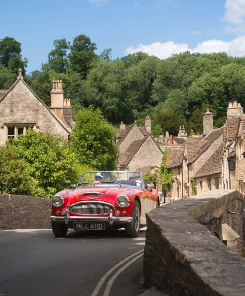A red vintage sports car driving over the bridge in the village of Castle Combe, near Bristol - credit Great West Way