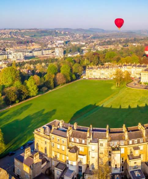An aerial view of the Royal Crescent in Bath near Bristol, with hot air balloons launching from the green