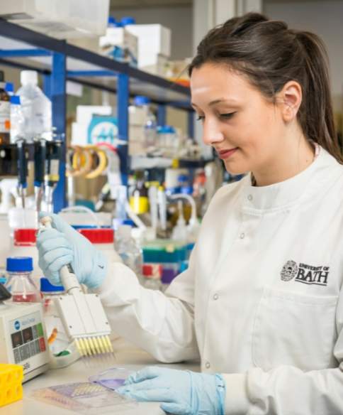 A women wearing a white lab coat with the University of Bath logo on it holding scientific equiptment