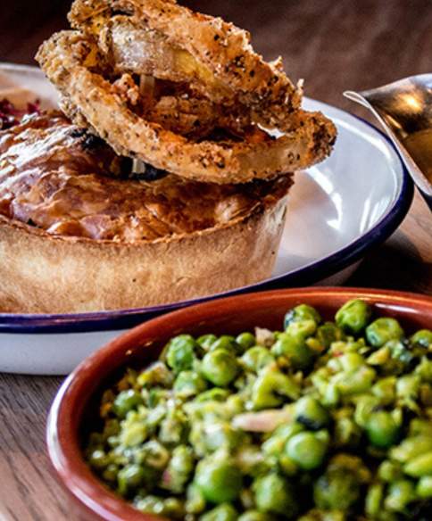 A pie and salad on a plate with a gravy boat and separate bowl of peas at Pieminister Bristol - credit Pieminister