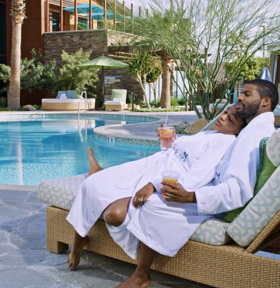 Man and woman relaxing together in lounge chair poolside with cool drinks in hands